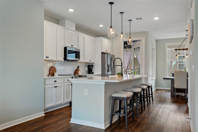 12330 Koshiba Aly, Orlando, FL 32827 - kitchen featuring dark wood finished floors, a center island with sink, stainless steel appliances, visible vents, and decorative backsplash