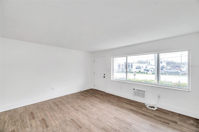 empty room with light wood-type flooring, a wall mounted air conditioner, and baseboards