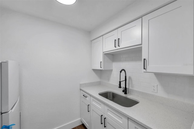 kitchen featuring a sink, backsplash, freestanding refrigerator, and white cabinetry