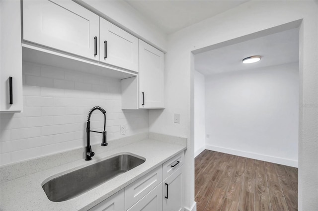 kitchen with tasteful backsplash, white cabinets, baseboards, a sink, and wood finished floors