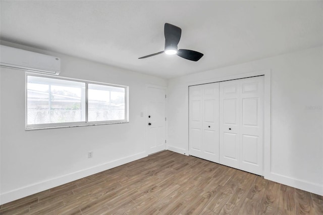 unfurnished bedroom featuring a wall mounted air conditioner, light wood-type flooring, baseboards, and a closet