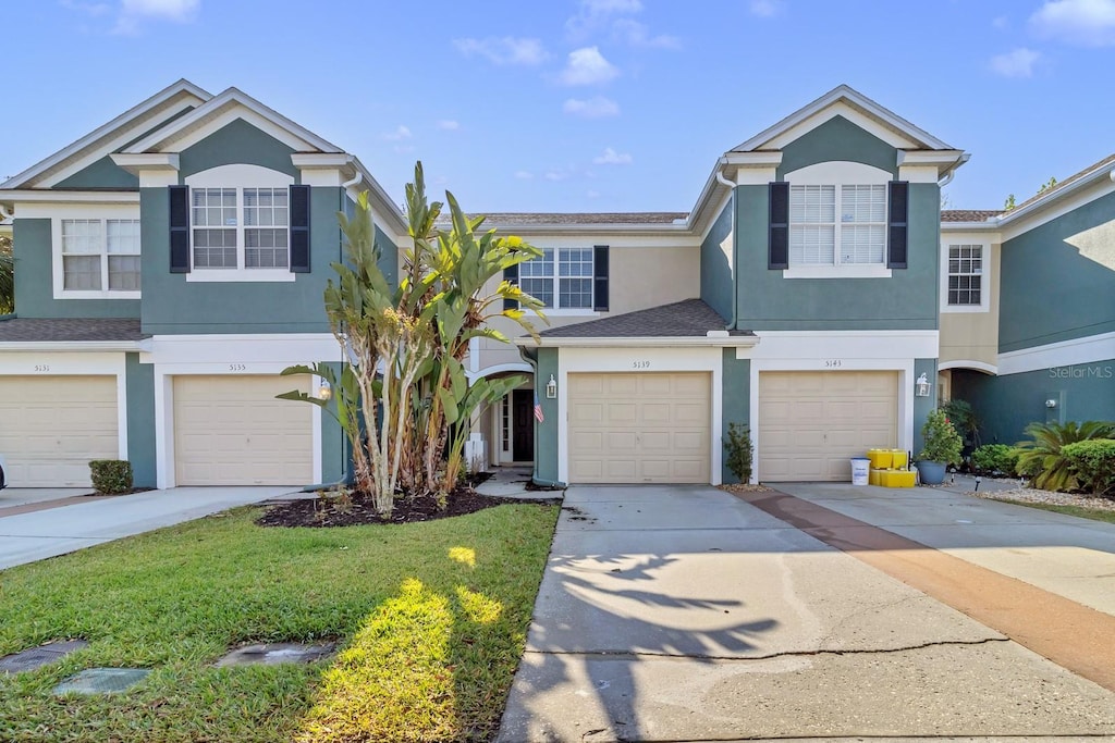 view of property featuring a front yard, a garage, concrete driveway, and stucco siding