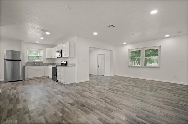 4385 Cassius St, Orlando, FL 32811 - kitchen with appliances with stainless steel finishes, open floor plan, wood finished floors, recessed lighting, and white cabinetry