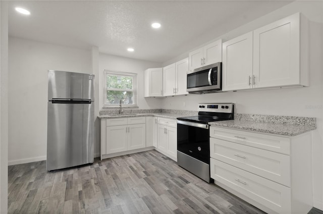 4385 Cassius St, Orlando, FL 32811 - kitchen featuring stainless steel appliances, a sink, light wood-style floors, white cabinetry, and light stone counters