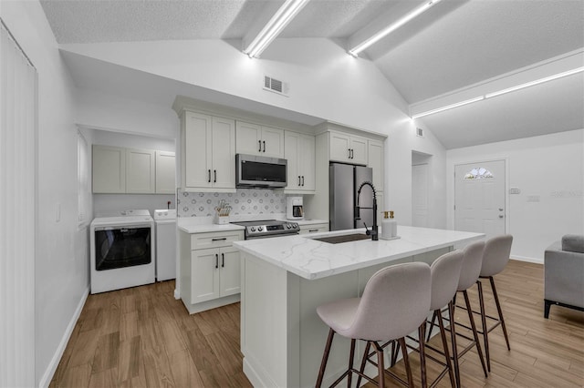 4066 Vanet Ct, Orlando, FL 32822 - kitchen with vaulted ceiling, washing machine and dryer, a sink, a kitchen bar, and stainless steel appliances