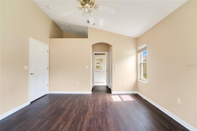 empty room featuring lofted ceiling, dark wood-style flooring, baseboards, arched walkways, and ceiling fan