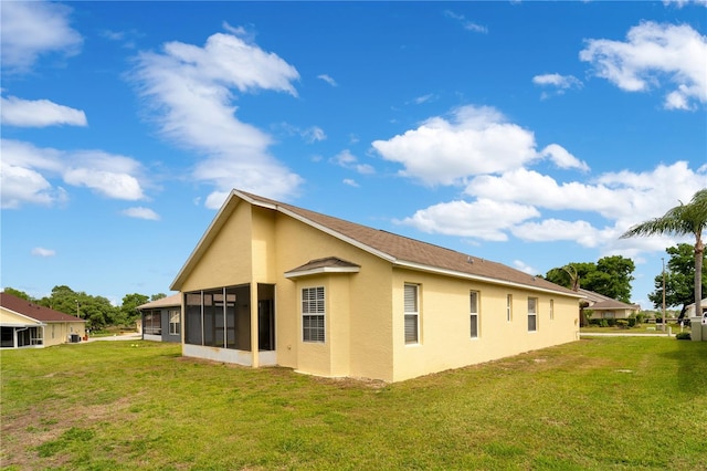 rear view of house featuring stucco siding, a sunroom, and a lawn