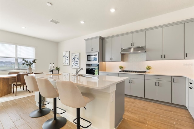 13231 Panama Beach Ct, Orlando, FL 32827 - kitchen with a sink, oven, gray cabinets, under cabinet range hood, and a breakfast bar
