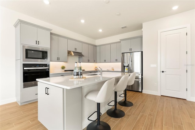 13231 Panama Beach Ct, Orlando, FL 32827 - kitchen with stainless steel appliances, under cabinet range hood, a sink, gray cabinets, and light wood finished floors