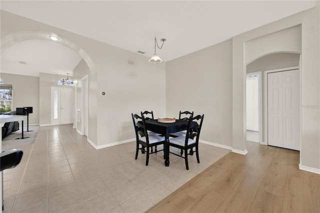 dining area with arched walkways, baseboards, light wood-style flooring, and visible vents