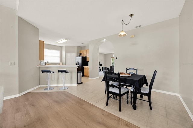 dining room with arched walkways, baseboards, light wood-style flooring, and visible vents