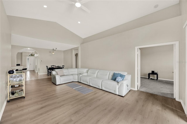 living area featuring vaulted ceiling, baseboards, arched walkways, ceiling fan, and light wood-style flooring