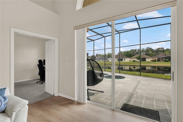 doorway to outside with a water view, a sunroom, wood finished floors, and plenty of natural light