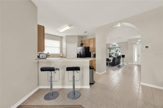 kitchen featuring arched walkways, black fridge with ice dispenser, a peninsula, and plenty of natural light