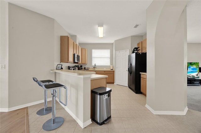 kitchen featuring black fridge, a peninsula, range, stainless steel microwave, and visible vents