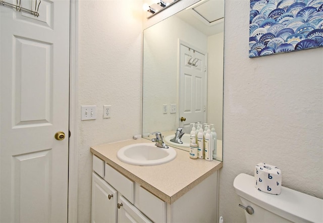 bathroom with toilet, vanity, and a textured wall