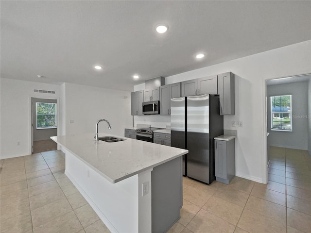 kitchen featuring visible vents, stainless steel appliances, a sink, an island with sink, and gray cabinetry