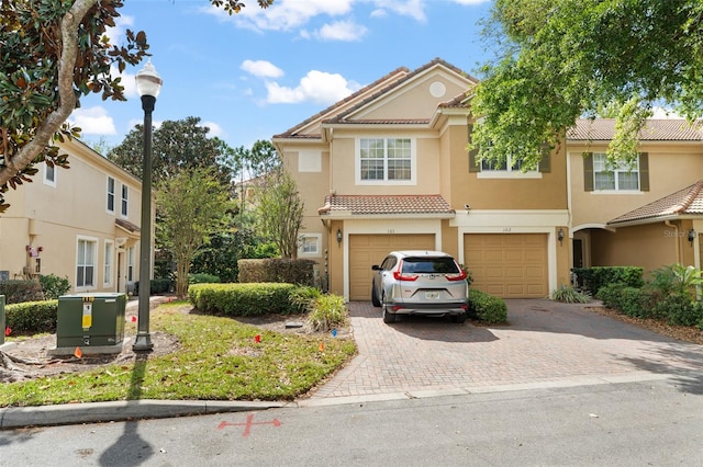view of front of property with a tile roof, decorative driveway, an attached garage, and stucco siding