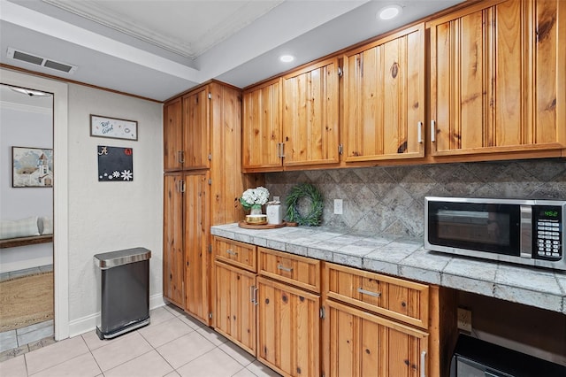 kitchen with stainless steel microwave, backsplash, visible vents, and ornamental molding