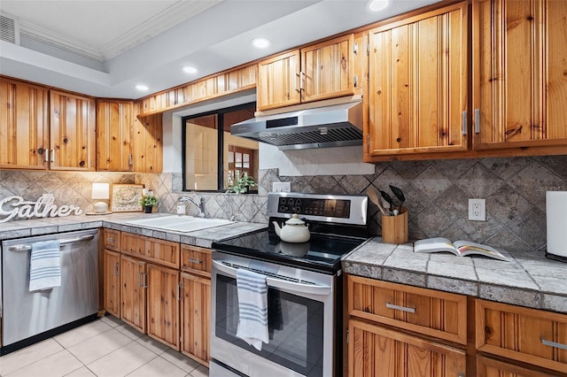 kitchen featuring recessed lighting, under cabinet range hood, a sink, crown molding, and appliances with stainless steel finishes