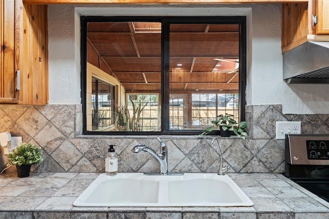kitchen with a textured wall, under cabinet range hood, tasteful backsplash, and a sink