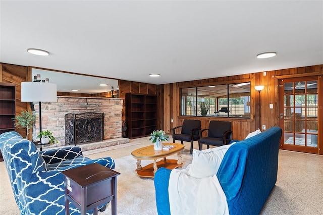 living room with a stone fireplace, carpet flooring, and wood walls