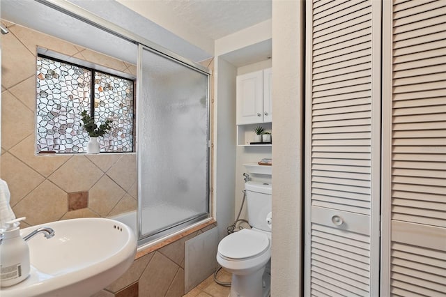 full bath featuring tile patterned floors, a sink, toilet, a closet, and combined bath / shower with glass door