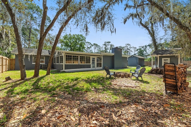 rear view of property featuring a shed, a fire pit, fence, an outbuilding, and a sunroom