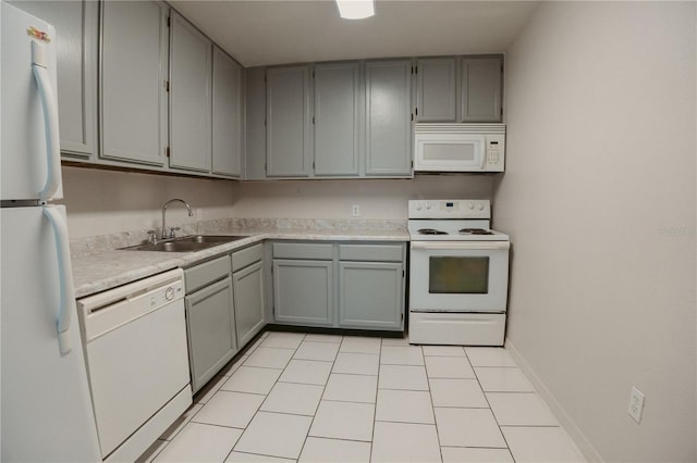 kitchen with light countertops, a sink, gray cabinetry, baseboards, and white appliances