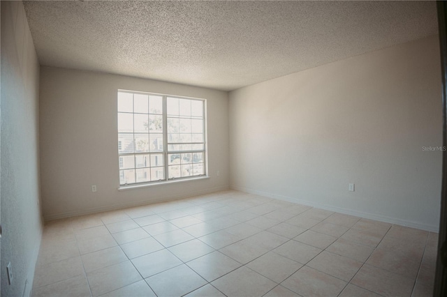 empty room with light tile patterned flooring, baseboards, and a textured ceiling