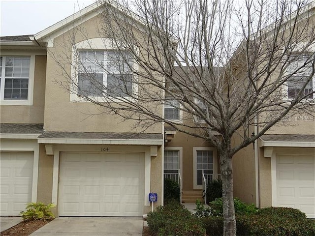 multi unit property with a shingled roof, driveway, stucco siding, and a garage