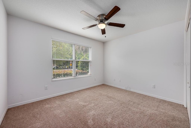 carpeted empty room featuring baseboards, ceiling fan, and a textured ceiling