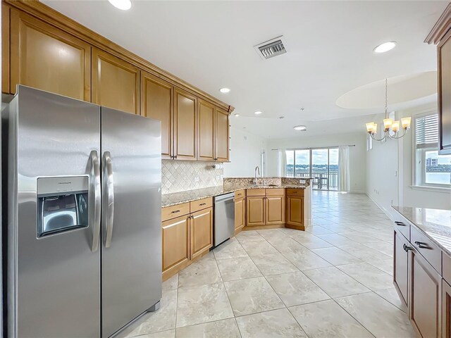 8743 S The Esplanade Unit 18, Orlando, FL 32836 - kitchen featuring stainless steel appliances, a peninsula, backsplash, a chandelier, and light stone countertops