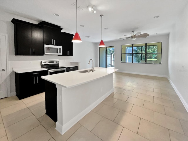 kitchen with light countertops, dark cabinetry, a sink, a kitchen island with sink, and appliances with stainless steel finishes