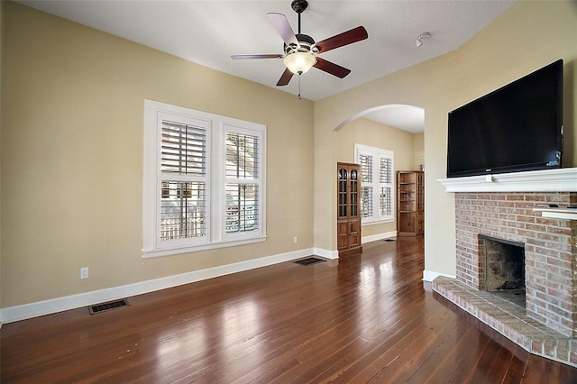 unfurnished living room with a brick fireplace, visible vents, arched walkways, ceiling fan, and hardwood / wood-style floors