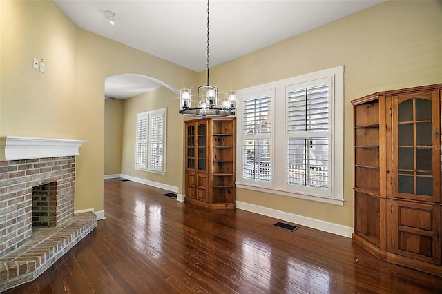 unfurnished dining area featuring wood-type flooring, baseboards, a chandelier, arched walkways, and visible vents