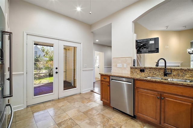 kitchen with french doors, stainless steel dishwasher, dark stone counters, a sink, and brown cabinetry