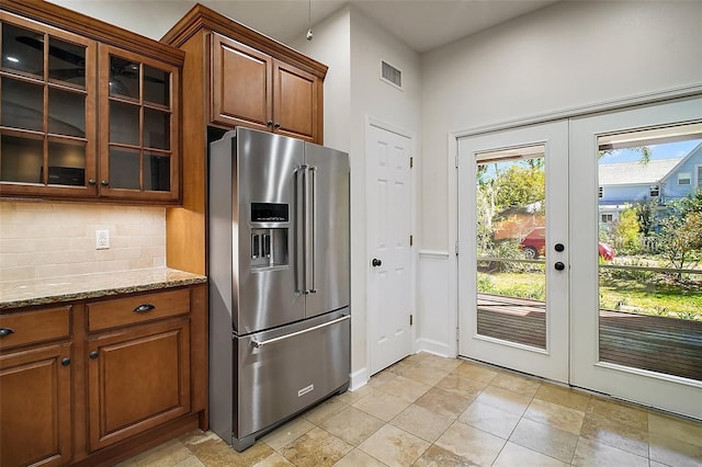 kitchen featuring light stone countertops, high quality fridge, glass insert cabinets, french doors, and backsplash