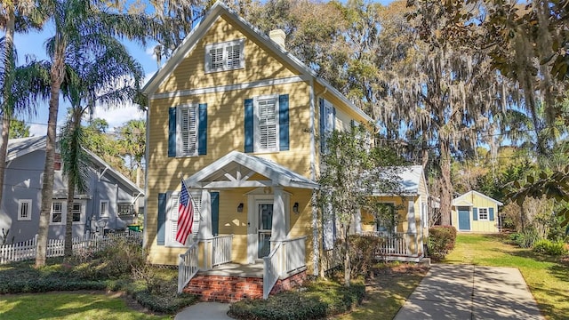 view of front of home with covered porch, fence, a front lawn, and a chimney