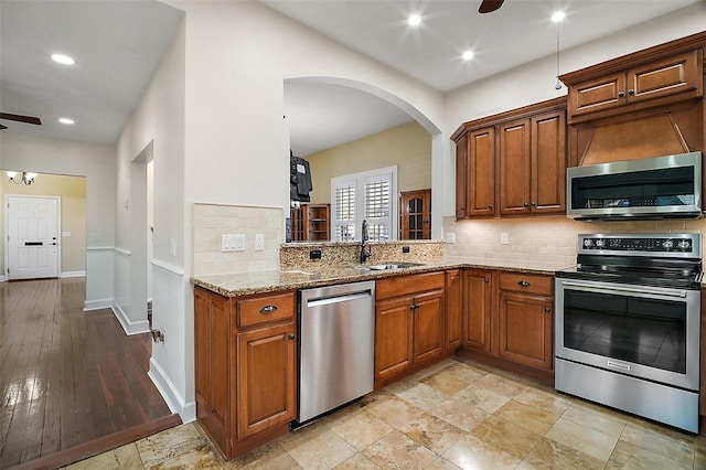 kitchen featuring a sink, a ceiling fan, light stone countertops, stainless steel appliances, and arched walkways