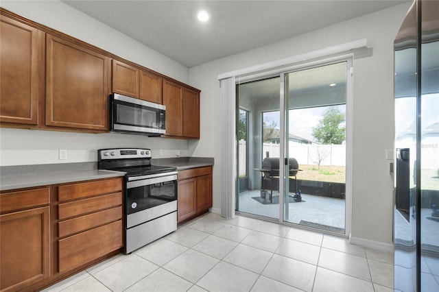 kitchen featuring brown cabinetry, light tile patterned flooring, baseboards, and stainless steel appliances