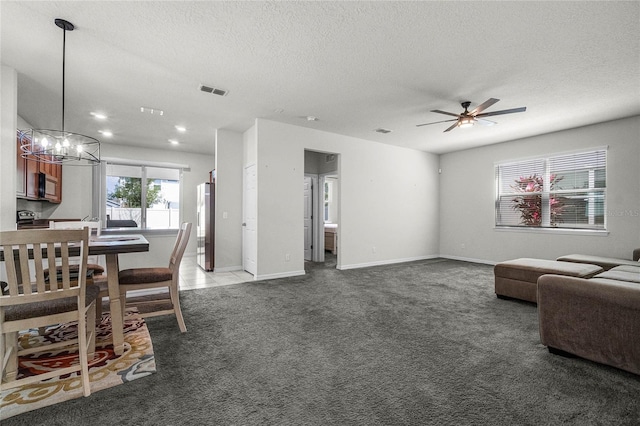 carpeted living area with baseboards, visible vents, ceiling fan with notable chandelier, and a textured ceiling