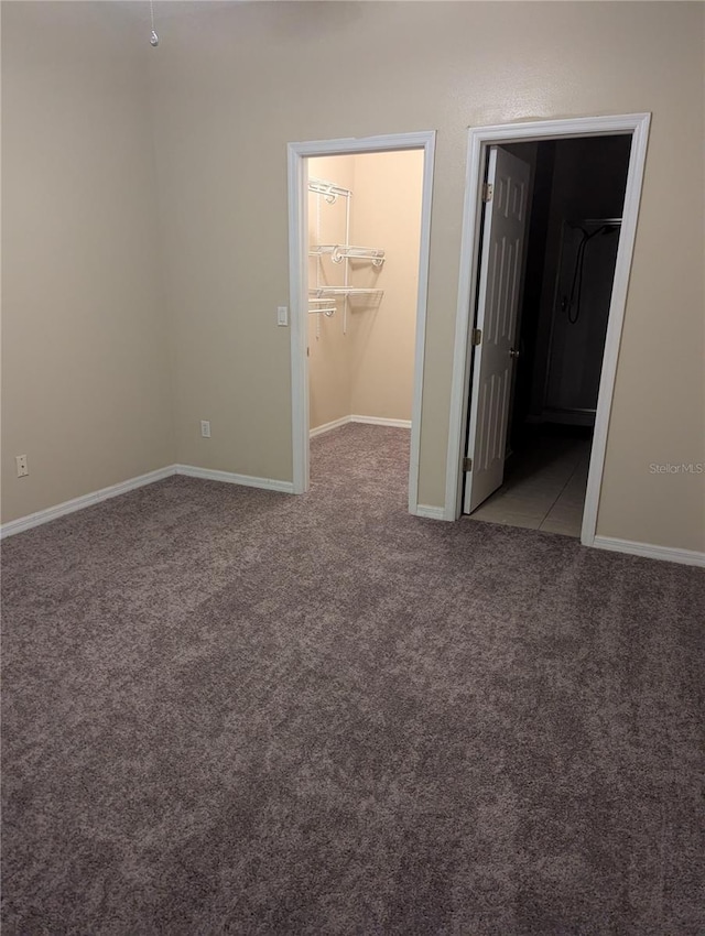 unfurnished bedroom with connected bathroom, carpet floors, baseboards, a spacious closet, and a closet