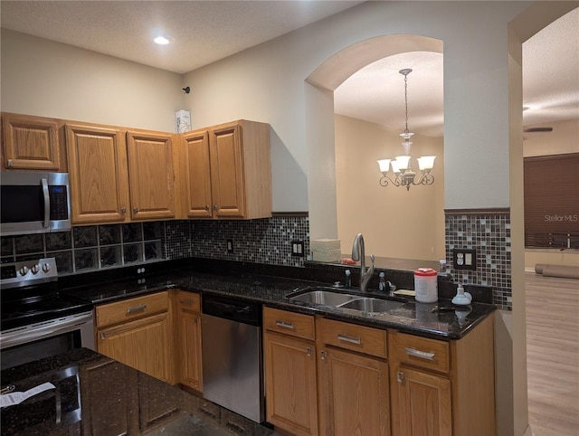 kitchen with appliances with stainless steel finishes, a sink, arched walkways, dark stone countertops, and tasteful backsplash