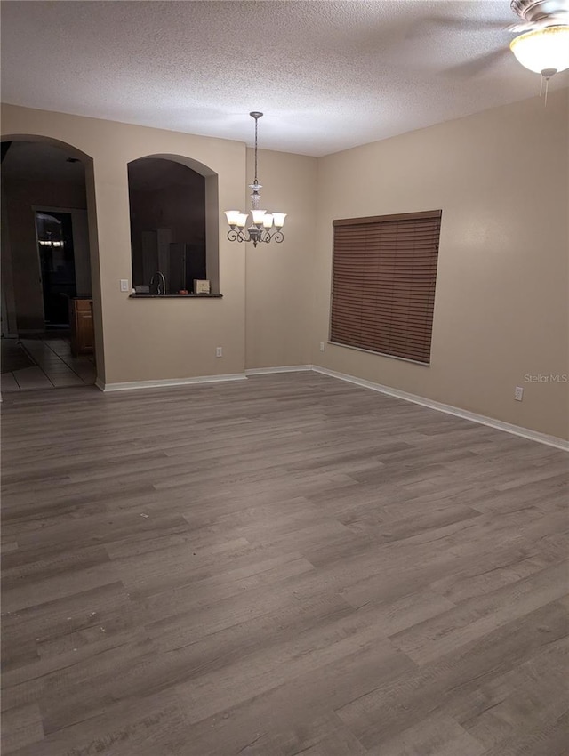 empty room with a textured ceiling, ceiling fan with notable chandelier, and wood finished floors