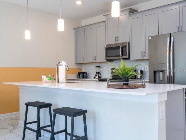 428 Ocean Course Ave, Davenport, FL 33896 - kitchen with stainless steel appliances, gray cabinetry, a sink, a kitchen breakfast bar, and decorative backsplash