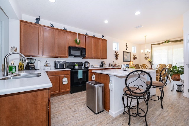 2289 Aloe Aly, Apopka, FL 32703 - kitchen featuring light wood finished floors, a kitchen island with sink, a sink, black appliances, and a breakfast bar area
