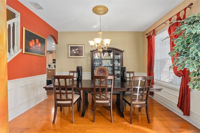 920 Nola Dr, Ocoee, FL 34761 - dining room featuring a chandelier, arched walkways, light wood-style flooring, plenty of natural light, and wainscoting
