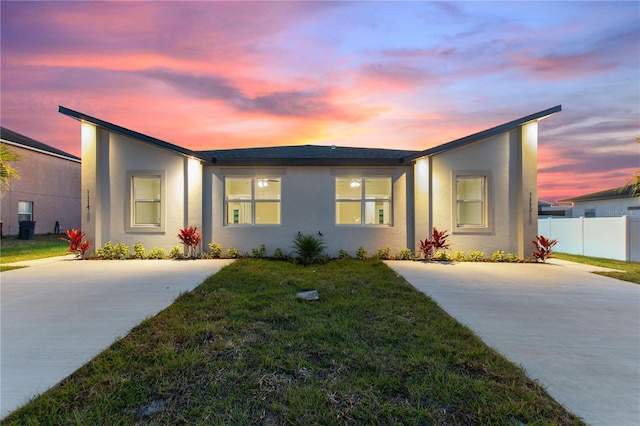 view of front of home with stucco siding, fence, and a yard