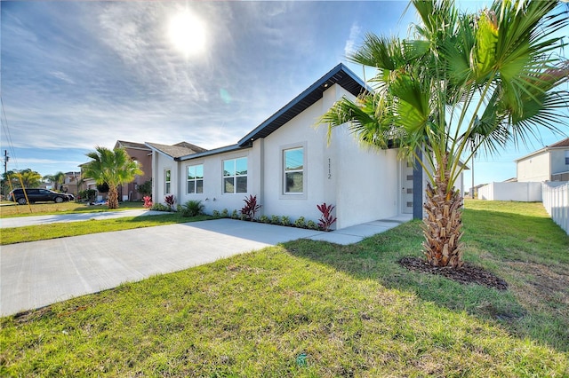 view of front of house featuring stucco siding, fence, and a front lawn